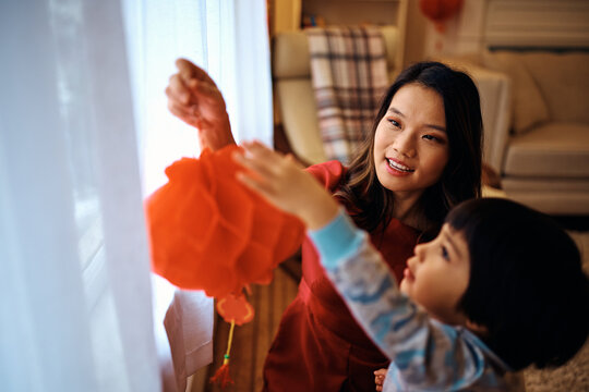 Chinese mother and son hanging traditional lanterns on windows while preparing for Luna New Year celebration.