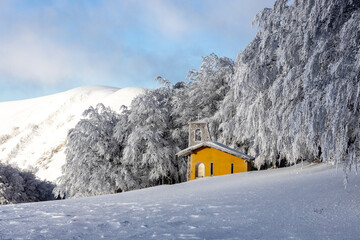 PIccola chiesa gialla in mezzo alla neve fresca sul Monte Nerone, Marche.