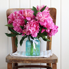 bouquet of pink peonies in a blue glass vase on an old chair