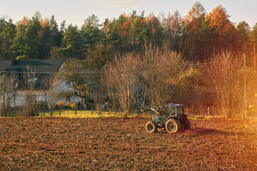 farm tractor on the soil field. busy rural area landscape. farmer working during golden hours