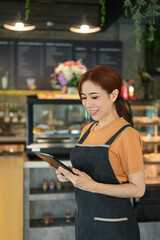 Portrait of female waitress standing standing in coffee shop and using digital tablet to checking reservations