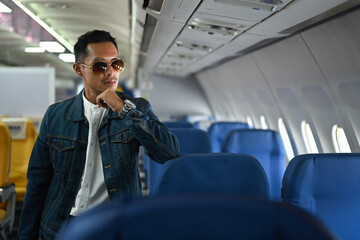 Portrait of hipster man traveller in sunglasses and jean jacket leaning on the airline seats