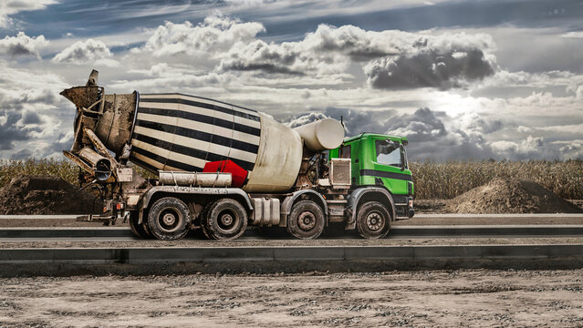 Concrete mixer truck at a construction site is driving down the road. Delivery of concrete for pouring foundations and building structures. Transportation of concrete.