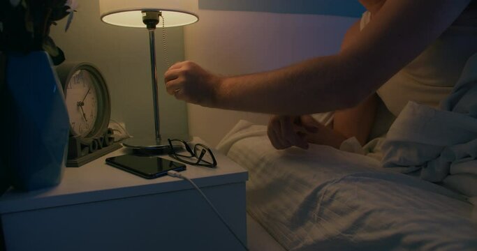 Young man put off eyewear and swith off light on nightstand and goes to sleep at night, medium close-up shot