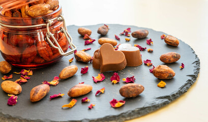 Chocolate heart and cocoa beans , with a jar filled with cocoa beans and rose petals on a slate plate