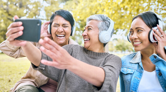 Senior woman, friends and phone laughing with headphones listening to music or watching comedy movie in the park. Group of happy elderly women enjoying funny series or 5G connection on smartphone