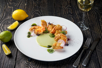 fried shrimp in batter in a plate with herbs and radish in a white plate on a black background with wine
