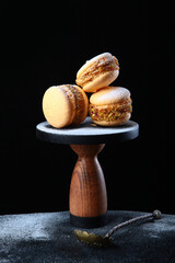Macarons cakes on wooden high stand. Vertical photo on a black background.