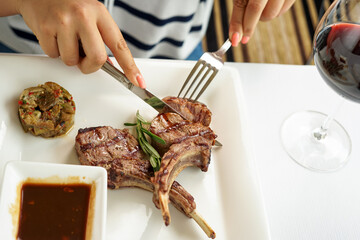 grilled meat loin in a square plate with sauce is cut with utensils in female hands
