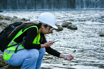 Environmental engineer uses a mobile phone to record water analysis data in dam. Environmentalists collect water samples from the dam to check for contamination. Water and ecology concept