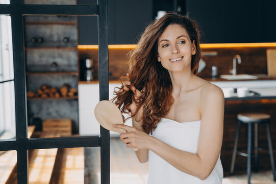 Young hispanic woman combs her long curly hair. Relaxation, grooming and pampering at home.