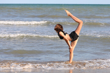 barefoot girl in black swimsuit from rhythmic gymnastics exercises on the seashore