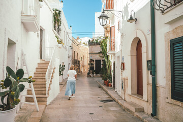 Woman walking down a pretty street with pot plants in Monopoli in Puglia, Italy