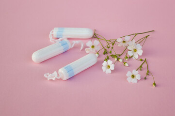 The concept of careful and gentle protection in critical days. Menstruation period concept. Hygienic white tampons for women with flowers on pink backround.