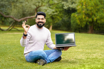 Obraz premium Young indian man showing laptop screen at park.