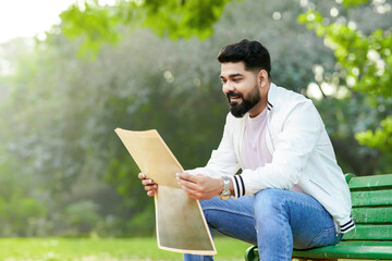 Young indian man reading news paper at park.