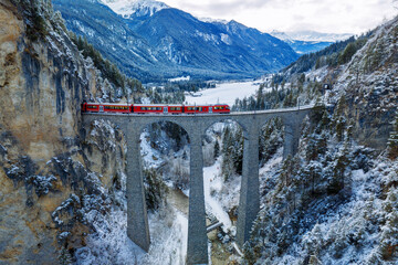 Aerial view of Train passing through famous mountain in Filisur, Switzerland. Landwasser Viaduct world heritage with train express in Swiss Alps snow winter scenery.