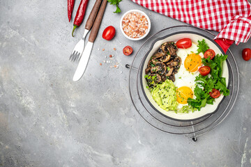 Fried scrambled eggs in a frying pan with avocado and mushrooms on a light background. Keto diet. top view. place for text