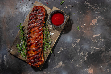 hot grilled spare ribs on cutting board on a dark background. American Spare Ribs in BBQ Sauce. Restaurant menu, dieting, cookbook recipe top view