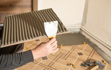 Worker using spatula and putting glue on ceramic tile.