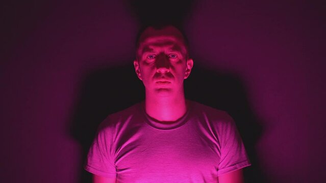 a man illuminated by red light stands against the wall and looks into the camera. High quality Full HD video recording