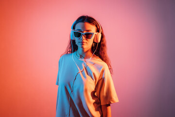 Obraz na płótnie Canvas Stylish teen hipster pretty fashion girl model wear glasses and headphones, enjoy and listen new dance music looking at camera at colorful studio background.