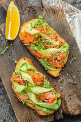 two toasts with salted salmon, guacamole avocado and fresh greens on plate. superfood concept. Healthy, clean eating. Vegan or gluten free diet. top view