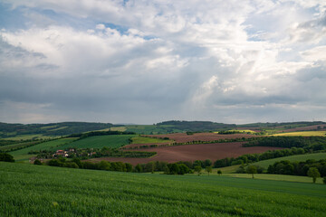 Hilly area in Saxony, near Dresden. Landscape with green fields and meadows. Houses are visible in the distance. Dark sky and many clouds. Before sunset.