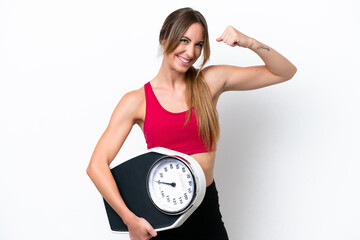 Young caucasian woman isolated on white background holding a weighing machine and doing strong...