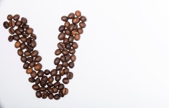V is a capital letter of the English alphabet made up of natural roasted coffee beans that lie on a white background. Plenty of space to put text or pictures, top view and studio photography.