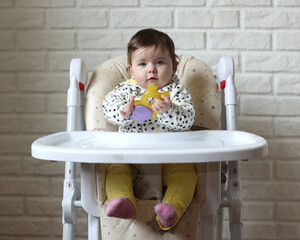 A little girl is sitting in a child's chair. The kid looks at everything with an interesting look