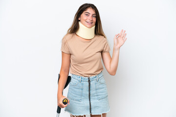 Young caucasian woman wearing neck brace and crutch isolated on white background saluting with hand...
