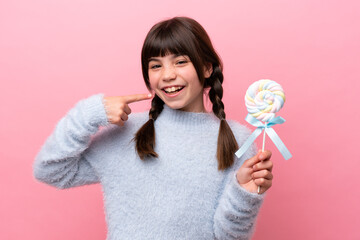 Little caucasian girl holding a lollipop giving a thumbs up gesture