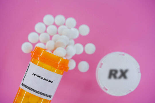 Levocetirizine Rx medicine pills in plactic vial with tablets. Pills spilling   from yellow container on pink background.