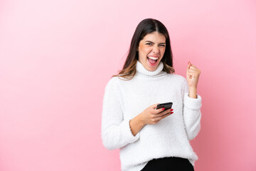 Young Italian woman isolated on pink background with phone in victory position