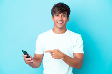 Young caucasian man isolated on blue background using mobile phone and pointing it