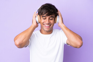 Fototapeta premium Young caucasian man isolated on purple background listening music