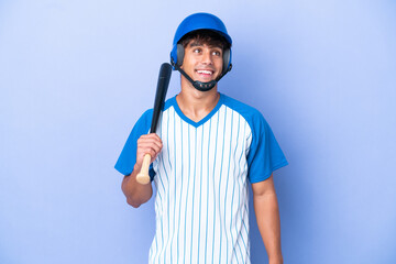 Baseball caucasian man player with helmet and bat isolated on blue background thinking an idea while looking up
