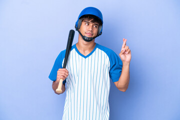 Baseball caucasian man player with helmet and bat isolated on blue background with fingers crossing and wishing the best