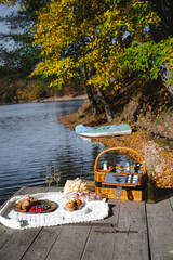 A cozy picnic setup by the lakeside features a woven basket filled with snacks and refreshments. Vibrant autumn leaves surround calm waters, creating a peaceful escape.