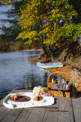 A cozy picnic setup by the lakeside features a woven basket filled with snacks and refreshments. Vibrant autumn leaves surround calm waters, creating a peaceful escape.