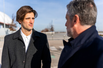 Pensive businessmen in smart clothes looking at each other while having conversation about work on sunny day