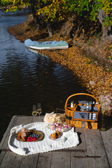 A cozy picnic setup by the lakeside features a woven basket filled with snacks and refreshments. Vibrant autumn leaves surround calm waters, creating a peaceful escape.