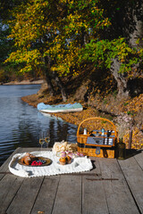 A cozy picnic setup by the lakeside features a woven basket filled with snacks and refreshments. Vibrant autumn leaves surround calm waters, creating a peaceful escape.