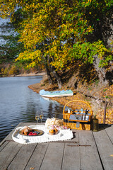 A cozy picnic setup by the lakeside features a woven basket filled with snacks and refreshments. Vibrant autumn leaves surround calm waters, creating a peaceful escape.