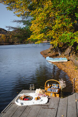 A cozy picnic setup by the lakeside features a woven basket filled with snacks and refreshments. Vibrant autumn leaves surround calm waters, creating a peaceful escape.