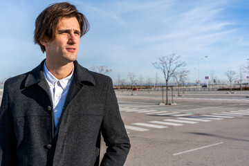 Thoughtful adult businessman in classy coat standing on street and looking away pensively while thinking about new startup project