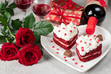 Obraz na płótnie Canvas Cakes Red velvet in the shape of hearts with whipped cream on white plate, roses and bottle wine for Valentines Day