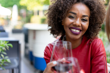 A beautiful African woman smiling and holding a glass of red wine. Despite diastema, her natural beauty shines through.  Diversity, inclusivity and friendship concept