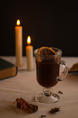 Cozy vintage composition with books, hot delicious mulled wine and candles on contrast background. Festive mood of a quiet evening.